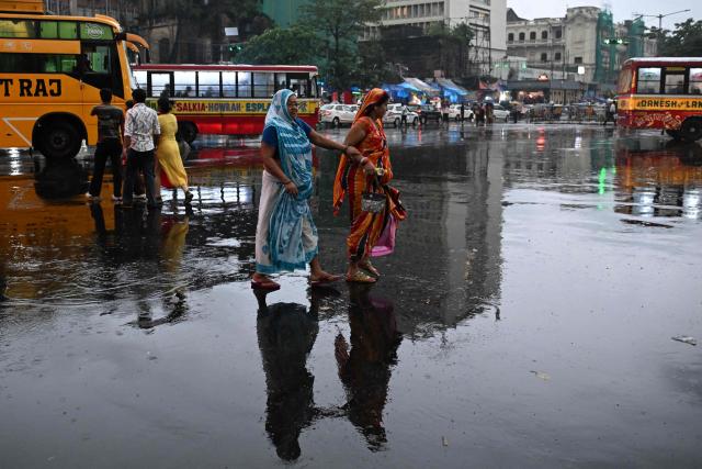 Pedestrians walk across a water-logged street during raifall in Kolkata on June 10, 2026. (Photo by Dibyangshu SARKAR / AFP)