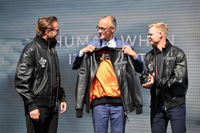 German Chancellor Friedrich Merz holds a leather jacket prior the unveiling of the PULSE P19 drone manufactured by German manufacturer of civil and military surveillance drones Quantum-Systems during his visit at the International Aerospace Exhibition (ILA) in Schoenefeld, near Berlin on June 10, 2026. (Photo by RALF HIRSCHBERGER / AFP)