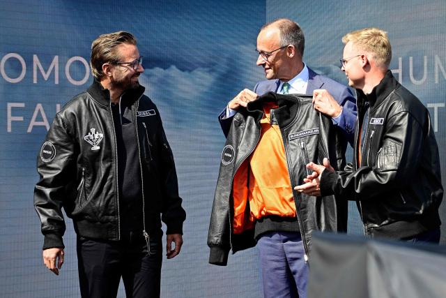 German Chancellor Friedrich Merz (C) holds a leather jacket presented to him prior the unveiling of the PULSE P19 drone manufactured by German manufacturer of civil and military surveillance drones Quantum-Systems during his visit at the International Aerospace Exhibition (ILA) in Schoenefeld, near Berlin on June 10, 2026. (Photo by Tobias SCHWARZ / AFP)