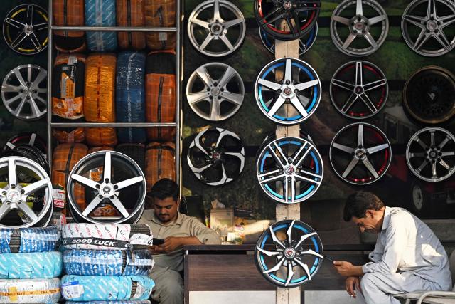 Shopkeepers selling tyres use mobile phones at a marketplace in Rawalpindi on June 10, 2026. (Photo by Farooq NAEEM / AFP)