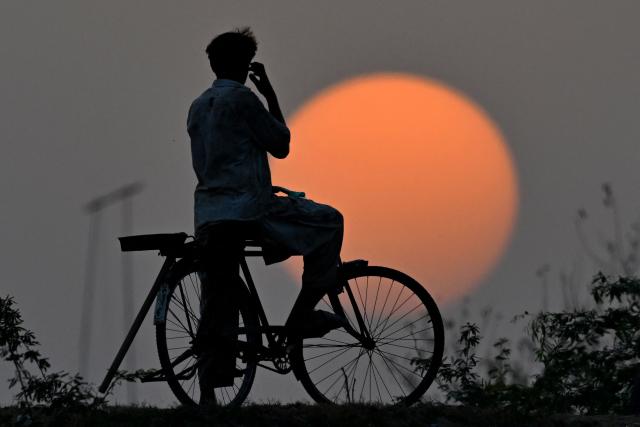 A man riding a bicycle looks on during the sunset on a hot summer day in Lahore on June 10, 2026. (Photo by Arif ALI / AFP)
