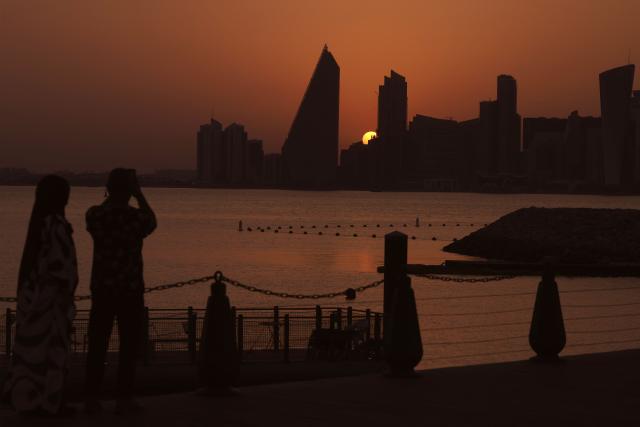People look on as the sun sets behind the Doha skyline on June 10, 2026. (Photo by Karim JAAFAR / AFP)
