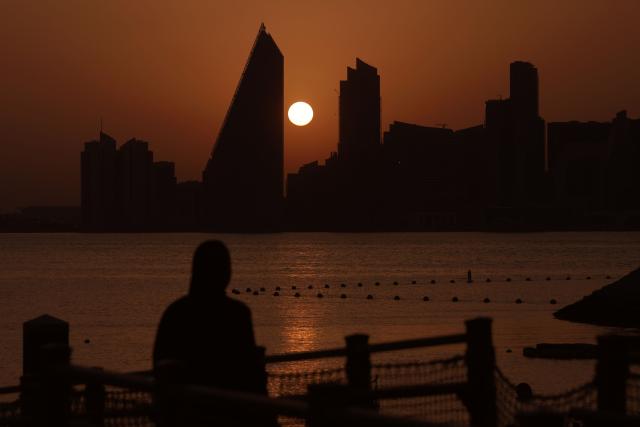 A person looks on as the sun sets behind the Doha skyline on June 10, 2026. (Photo by Karim JAAFAR / AFP)