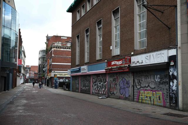 People walk past closed, shuttered shops in Belfast, Northern Ireland, on June 10, 2026. Northern Ireland braced Wednesday for a potential second night of violence directed at immigrants, following unrest that UK authorities say was stoked by far-right activists on social media after a brutal Belfast stabbing. (Photo by Henry NICHOLLS / AFP)