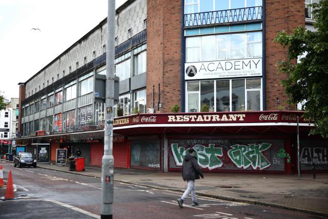People walk past closed, shuttered shops in Belfast, Northern Ireland, on June 10, 2026. Northern Ireland braced Wednesday for a potential second night of violence directed at immigrants, following unrest that UK authorities say was stoked by far-right activists on social media after a brutal Belfast stabbing. (Photo by Henry NICHOLLS / AFP)