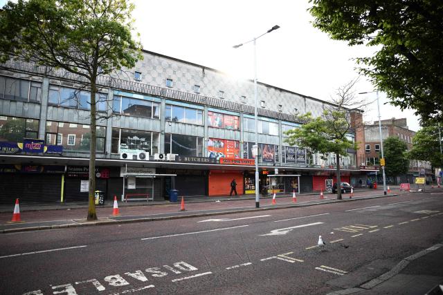 People walk past closed, shuttered shops in Belfast, Northern Ireland, on June 10, 2026. Northern Ireland braced Wednesday for a potential second night of violence directed at immigrants, following unrest that UK authorities say was stoked by far-right activists on social media after a brutal Belfast stabbing. (Photo by Henry NICHOLLS / AFP)
