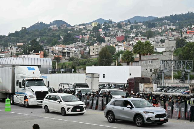 Police stand guard during an operation that keeps retained buses transporting students from Ayotzinapa who try to enter the city and join the protests of teachers and relatives of missing people ahead of the start of the 2026 FIFA World Cup, on the outskirts of Mexico City, on June 10, 2026. (Photo by YURI CORTEZ / AFP)