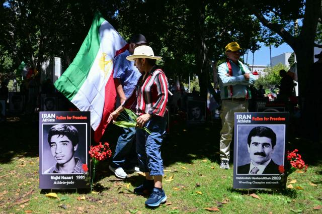 Demonstrators leave flowers by pictures of former Iranian athletes during a press conference held by the National Council of Resistance of Iran, who is calling on FIFA to suspend and expel the Iranian regime-controlled "Football Federation Islamic Republic of Iran" from international football, at Los Angeles City Hall, in Los Angeles, on June 10, 2026. (Photo by Frederic J. Brown / AFP)