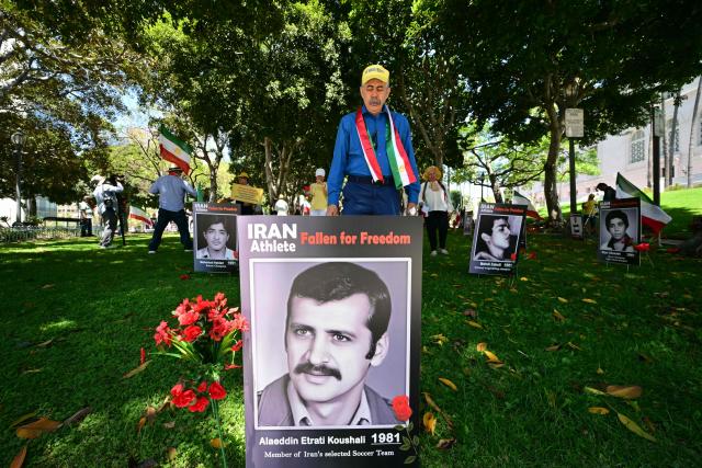 Demonstrators walk near pictures of former Iranian athletes during a press conference held by the National Council of Resistance of Iran, who is calling on FIFA to suspend and expel the Iranian regime-controlled "Football Federation Islamic Republic of Iran" from international football, at Los Angeles City Hall, in Los Angeles, on June 10, 2026. (Photo by Frederic J. Brown / AFP)