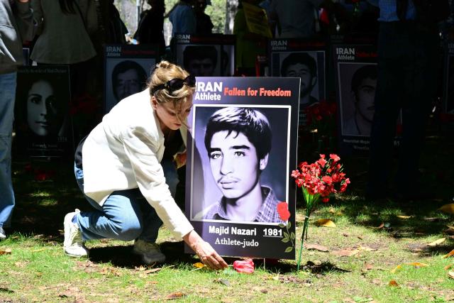A woman places a flower in front of a portrait of a late Iranian athlete, reading "fallen for freedom", after a press conference held by the National Council of Resistance of Iran, which is calling on FIFA to suspend and expel the Iranian regime-controlled "Football Federation Islamic Republic of Iran" from international football, at Los Angeles City Hall, in Los Angeles, on June 10, 2026. (Photo by Frederic J. Brown / AFP)