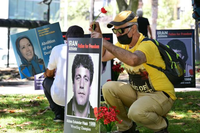 A man places a flower at the portrait of a late Iranian athlete, reading "fallen for freedom", after a press conference held by the National Council of Resistance of Iran, which is calling on FIFA to suspend and expel the Iranian regime-controlled "Football Federation Islamic Republic of Iran" from international football, at Los Angeles City Hall, in Los Angeles, on June 10, 2026. (Photo by Frederic J. Brown / AFP)