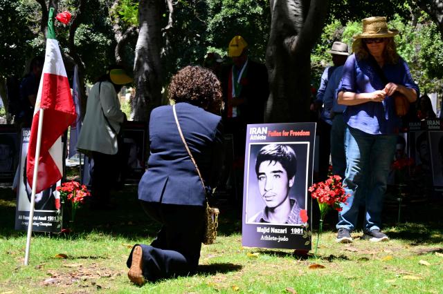 A woman kneels by the portrait of a late Iranian athlete, reading "fallen for freedom", after a press conference held by the National Council of Resistance of Iran, which is calling on FIFA to suspend and expel the Iranian regime-controlled "Football Federation Islamic Republic of Iran" from international football, at Los Angeles City Hall, in Los Angeles, on June 10, 2026. (Photo by Frederic J. Brown / AFP)