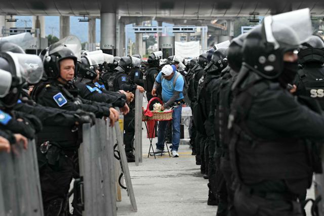 A vendor sells tacos to police officers standing guard during an operation that keeps retained buses transporting students from Ayotzinapa who try to enter the city and join the protests of teachers and relatives of missing people ahead of the start of the 2026 FIFA World Cup, on the outskirts of Mexico City, on June 10, 2026. (Photo by YURI CORTEZ / AFP)