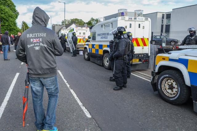 Police (R) in riot gear seal off a hotel previously believed to house migrants from protesters, in the town of Mallusk, Co Antrim, north of Belfast, Northern Ireland, on June 10, 2026. Northern Ireland braced on June 10 for a potential second night of violence directed at immigrants, following unrest that UK authorities say was stoked by far-right activists on social media after a brutal Belfast stabbing. (Photo by Paul Faith / AFP)
