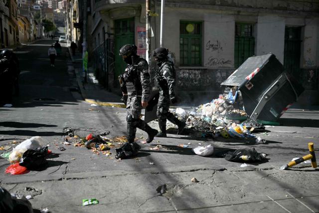 Riot police officers walk past an overturned garbage container in the middle of a street during a protest against the government of Bolivia's President Rodrigo Paz in La Paz on June 10, 2026. For weeks, protesters demanding that US-backed conservative President Rodrigo Paz's fledgling government address a deep economic crisis, while others called for his resignation, have marched and set up roadblocks, bringing Bolivia to a near standstill, driving up food and fuel prices and causing shortages of basic goods. (Photo by Marvin RECINOS / AFP)