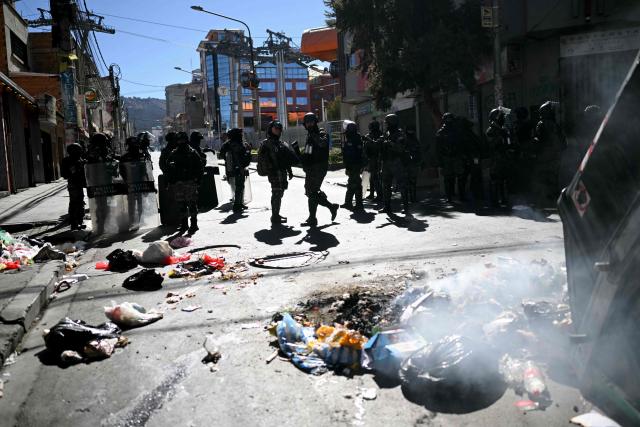 Riot police officers walk in front of an overturned garbage container in the middle of a street during a protest against the government of Bolivia's President Rodrigo Paz in La Paz on June 10, 2026. For weeks, protesters demanding that US-backed conservative President Rodrigo Paz's fledgling government address a deep economic crisis, while others called for his resignation, have marched and set up roadblocks, bringing Bolivia to a near standstill, driving up food and fuel prices and causing shortages of basic goods. (Photo by Marvin RECINOS / AFP)