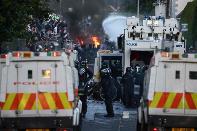 Police use water cannon as protesters (behind) gather near a hotel previously believed to house migrants, in the town of Mallusk, Co Antrim, north of Belfast, Northern Ireland, on June 10, 2026. Northern Ireland braced on June 10 for a potential second night of violence directed at immigrants, following unrest that UK authorities say was stoked by far-right activists on social media after a brutal Belfast stabbing. (Photo by Henry NICHOLLS / AFP)