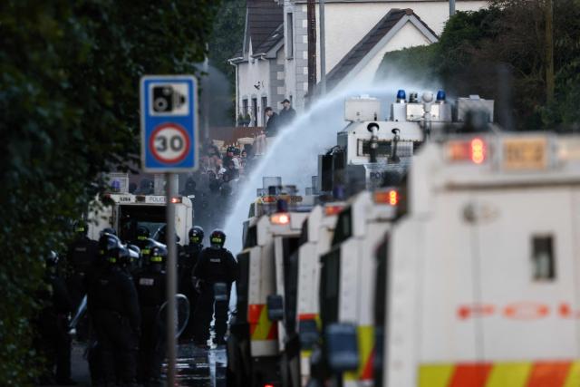 Police use water cannon as protesters (behind) gather near a hotel previously believed to house migrants, in the town of Mallusk, Co Antrim, north of Belfast, Northern Ireland, on June 10, 2026. Northern Ireland braced on June 10 for a potential second night of violence directed at immigrants, following unrest that UK authorities say was stoked by far-right activists on social media after a brutal Belfast stabbing. (Photo by Henry NICHOLLS / AFP)