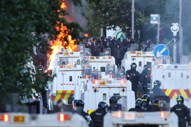Protesters (behind) stand off with police in Glengormley, north of Belfast, Northern Ireland, on June 10, 2026. Police used water cannon late on June 10 to disperse small crowds who had gathered for a second night in Northern Ireland as UK authorities blamed far-right activists for stoking anger on social media following a brutal stabbing. (Photo by Paul Faith / AFP)