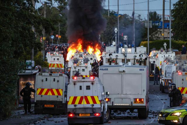Fires burn as protesters (behind) stand off with police in Glengormley, north of Belfast, Northern Ireland, on June 10, 2026. Police used water cannon late on June 10 to disperse small crowds who had gathered for a second night in Northern Ireland as UK authorities blamed far-right activists for stoking anger on social media following a brutal stabbing. (Photo by Henry NICHOLLS / AFP)