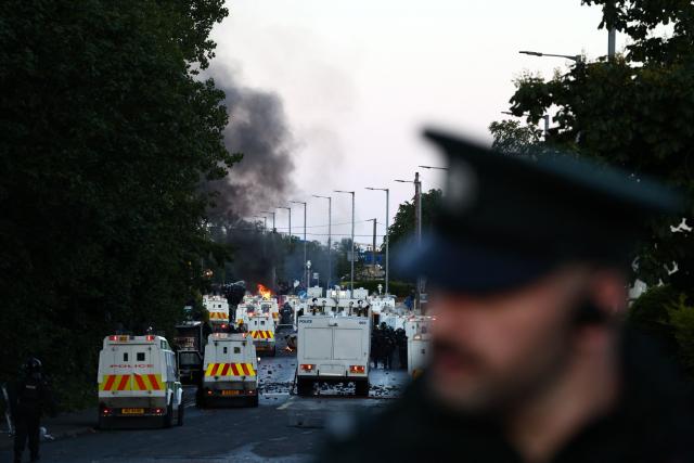 Fires burn as protesters (behind) stand off with police in Glengormley, north of Belfast, Northern Ireland, on June 10, 2026. Police used water cannon late on June 10 to disperse small crowds who had gathered for a second night in Northern Ireland as UK authorities blamed far-right activists for stoking anger on social media following a brutal stabbing. (Photo by Henry NICHOLLS / AFP)