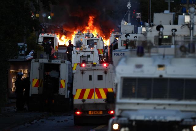 Fires burn as protesters (behind) stand off with police in Glengormley, north of Belfast, Northern Ireland, on June 10, 2026. Police used water cannons late on June 10 to disperse small crowds who had gathered for a second night in Northern Ireland as UK authorities blamed far-right activists for stoking anger on social media following a brutal stabbing. (Photo by Henry NICHOLLS / AFP)