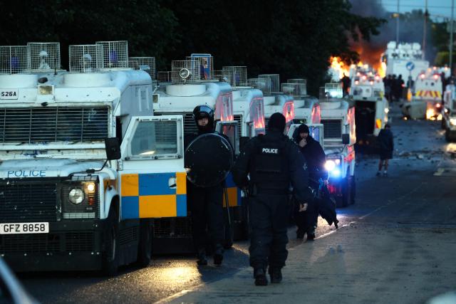 Fires burn as protesters (behind) stand off with police in Glengormley, north of Belfast, Northern Ireland, on June 10, 2026. Police used water cannons late on June 10 to disperse small crowds who had gathered for a second night in Northern Ireland as UK authorities blamed far-right activists for stoking anger on social media following a brutal stabbing. (Photo by Henry NICHOLLS / AFP)