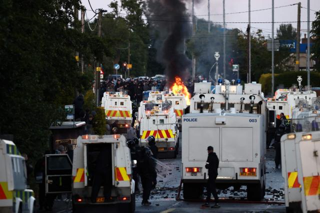 Debris from items thrown at police is pictured in the road amidst police vans, as fires burn while protesters (behind) stand off with police on Antrim Road in Glengormley, north of Belfast, Northern Ireland, on June 10, 2026. Police used water cannons late on June 10 to disperse small crowds who had gathered for a second night in Northern Ireland as UK authorities blamed far-right activists for stoking anger on social media following a brutal stabbing. (Photo by Henry NICHOLLS / AFP)