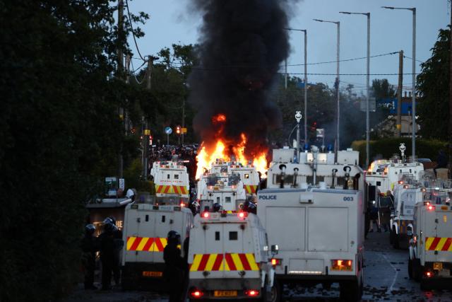 Fires burn as protesters (behind) stand off with police on Atrim Road in Glengormley, north of Belfast, Northern Ireland, on June 10, 2026. Police used water cannons late on June 10 to disperse small crowds who had gathered for a second night in Northern Ireland as UK authorities blamed far-right activists for stoking anger on social media following a brutal stabbing. (Photo by Henry NICHOLLS / AFP)