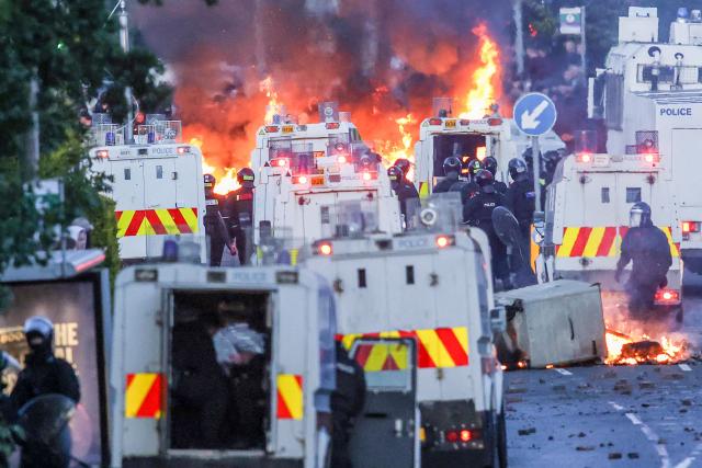 Fires burn around police vehicles as protesters (behind) stand off with police in Glengormley, north of Belfast, Northern Ireland, on June 10, 2026. Police used water cannon late on June 10 to disperse small crowds who had gathered for a second night in Northern Ireland as UK authorities blamed far-right activists for stoking anger on social media following a brutal stabbing. (Photo by Paul Faith / AFP)