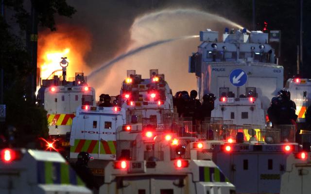 Police use a water cannon as they block the road from protesters (behind) leading to a hotel previously believed to house migrants, on Antrim Road in Glengormley, north of Belfast, Northern Ireland, on June 10, 2026. Police used water cannons late on June 10 to disperse small crowds who had gathered for a second night in Northern Ireland as UK authorities blamed far-right activists for stoking anger on social media following a brutal stabbing. (Photo by Henry NICHOLLS / AFP)