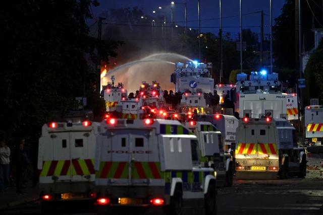Police use a water cannon as they block the road from protesters (behind) leading to a hotel previously believed to house migrants, on Antrim Road in Glengormley, north of Belfast, Northern Ireland, on June 10, 2026. Police used water cannons late on June 10 to disperse small crowds who had gathered for a second night in Northern Ireland as UK authorities blamed far-right activists for stoking anger on social media following a brutal stabbing. (Photo by Henry NICHOLLS / AFP)