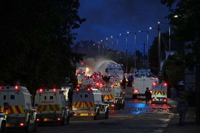 Police use a water cannon as they block the road from protesters (behind) leading to a hotel previously believed to house migrants, on Antrim Road in Glengormley, north of Belfast, Northern Ireland, on June 10, 2026. Police used water cannons late on June 10 to disperse small crowds who had gathered for a second night in Northern Ireland as UK authorities blamed far-right activists for stoking anger on social media following a brutal stabbing. (Photo by Henry NICHOLLS / AFP)