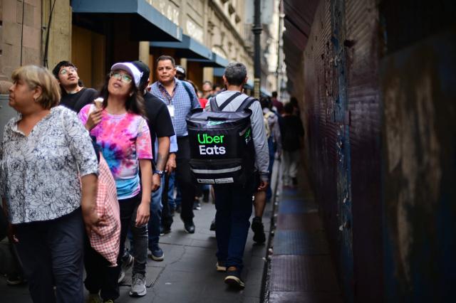 People walk past a security barrier set up to block access to the Fan Fest at Mexico City's Zocalo square on June 10, 2026, amid a threatened protest by the National Coordinator of Education Workers (CNTE) ahead of the 2026 FIFA World Cup. (Photo by Marco Antonio MARTINEZ / AFP)