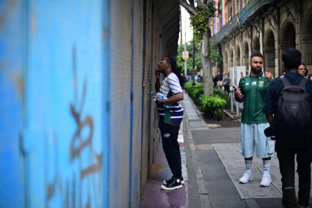 A man looks through a security barrier set up to block access to the Fan Fest at Mexico City's Zocalo square on June 10, 2026, amid a threatened protest by the National Coordinator of Education Workers (CNTE) ahead of the 2026 FIFA World Cup. (Photo by Marco Antonio MARTINEZ / AFP)