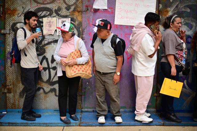 People stand next to a security barrier set up to block access to the Fan Fest at Mexico City's Zocalo square on June 10, 2026, amid a threatened protest by the National Coordinator of Education Workers (CNTE) ahead of the 2026 FIFA World Cup. (Photo by Marco Antonio MARTINEZ / AFP)