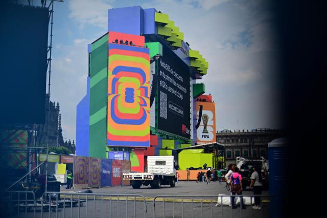 The giant screen of the Fan Fest is seen through a security barrier blocking access at Mexico City's Zocalo square on June 10, 2026, amid a threatened protest by the National Coordinator of Education Workers (CNTE) ahead of the 2026 FIFA World Cup. (Photo by Marco Antonio MARTINEZ / AFP)