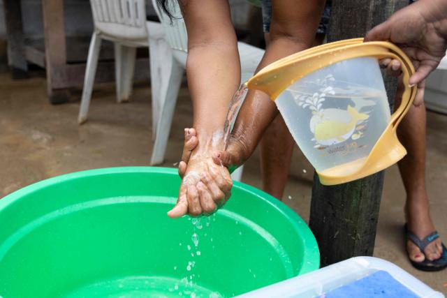 A resident washes her hands before treating water from her well, as part of the Home Water Treatment project — known by its French acronym TED (Traitement de l'Eau а Domicile) — in the Savane district of Matoury, French Guiana, on June 6, 2026. Launched as a pilot in 2025 within the regional health agency's (ARS) 2024–2028 environmental health plan, the TED project supports families who lack secure access to drinking water, teaching them simple, low-cost methods — chiefly chlorination and proper storage — to cut the health risks of consuming untreated water. In French Guiana, around 15 percent of the population is not connected to the public drinking-water network, drawing instead on rainwater, wells, creeks or rivers. The approach relies on door-to-door support: meetings with families, practical demonstrations, tailored advice and home follow-up. (Photo by Ronan LIЙTAR / AFP)