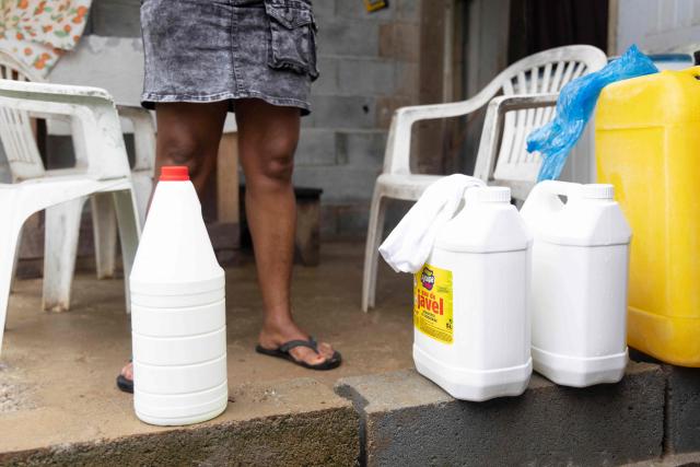 This photograph shows cans of a chlorine solution used to treat water and make it safer to drink, used as part of the Home Water Treatment project — known by its French acronym TED (Traitement de l'Eau а Domicile) in the Savane district of Matoury, French Guiana, on June 6, 2026. Launched as a pilot in 2025 within the regional health agency's (ARS) 2024–2028 environmental health plan, the TED project supports families who lack secure access to drinking water, teaching them simple, low-cost methods — chiefly chlorination and proper storage — to cut the health risks of consuming untreated water. In French Guiana, around 15 percent of the population is not connected to the public drinking-water network, drawing instead on rainwater, wells, creeks or rivers. The approach relies on door-to-door support: meetings with families, practical demonstrations, tailored advice and home follow-up. (Photo by Ronan LIЙTAR / AFP)