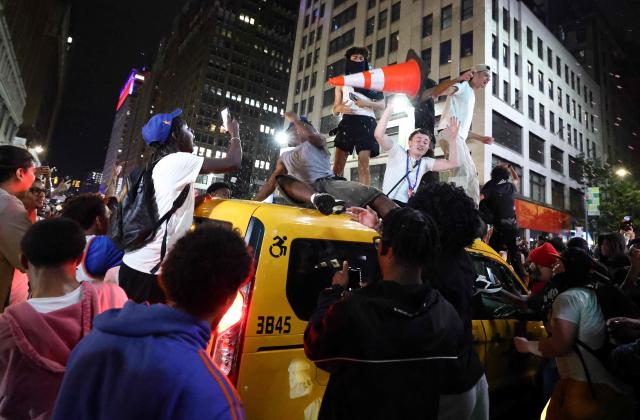 New York Knicks fans climb on a taxi as they celebrate outside Madison Square Garden after their team’s Game 4 victory over the San Antonio Spurs in the NBA Finals in New York on June 10, 2026. (Photo by CHARLY TRIBALLEAU / AFP)