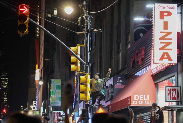 A New York Knicks fan hangs from a traffic light as he celebrates outside Madison Square Garden after his team’s Game 4 victory over the San Antonio Spurs in the NBA Finals in New York on June 10, 2026. (Photo by CHARLY TRIBALLEAU / AFP)