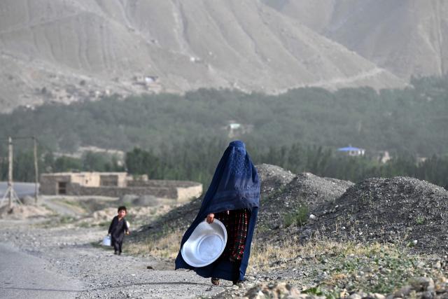 An Afghan burqa-clad woman carrying a large utensil walks along a street in Argo district of Afghanistan's Badakhshan province on June 10, 2026. (Photo by OMER ABRAR / AFP)
