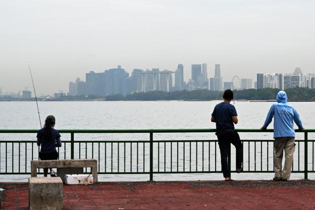 Anglers fish from a jetty overlooking the city skyline at East Coast Park in Singapore on June 11, 2026. (Photo by Roslan RAHMAN / AFP)