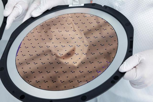 An employee holds a 300mm wafer at the new Smart Power Fab of German semiconductor manufacturer Infineon Technologies AG in Dresden, eastern Germany, on June 10, 2026. On July 2, 2026, Infineon will officially open its Smart Power Fab that manufactures power semiconductors as well as analog/mixed-signal-components in Dresden. With an investment of five billion euros, the new facility represents the largest single investment in Infineon's history. (Photo by Jens SCHLÜTER / AFP)