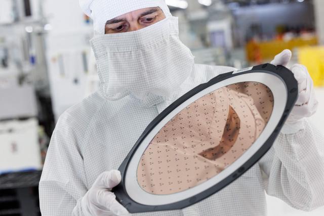 An employee holds a 300mm wafer at the new Smart Power Fab of German semiconductor manufacturer Infineon Technologies AG in Dresden, eastern Germany, on June 10, 2026. On July 2, 2026, Infineon will officially open its Smart Power Fab that manufactures power semiconductors as well as analog/mixed-signal-components in Dresden. With an investment of five billion euros, the new facility represents the largest single investment in Infineon's history. (Photo by Jens SCHLÜTER / AFP)
