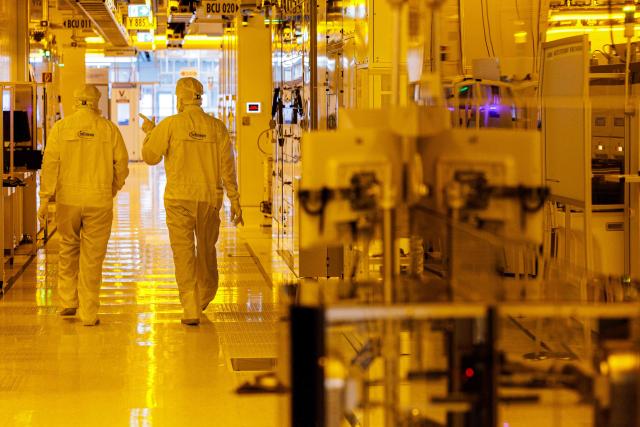 Two employees walk at the clean room for 300mm wafer manufacturing at the plant of German semiconductor manufacturer Infineon Technologies AG in Dresden, eastern Germany, on June 10, 2026. On July 2, 2026, Infineon will officially open its Smart Power Fab that manufactures power semiconductors as well as analog/mixed-signal-components in Dresden. With an investment of five billion euros, the new facility represents the largest single investment in Infineon's history. (Photo by Jens SCHLÜTER / AFP)
