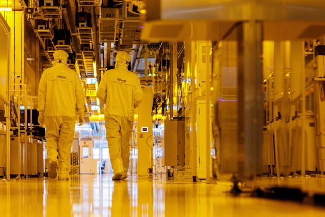 Two employees walk at the clean room for 300mm wafer manufacturing at the plant of German semiconductor manufacturer Infineon Technologies AG in Dresden, eastern Germany, on June 10, 2026. On July 2, 2026, Infineon will officially open its Smart Power Fab that manufactures power semiconductors as well as analog/mixed-signal-components in Dresden. With an investment of five billion euros, the new facility represents the largest single investment in Infineon's history. (Photo by Jens SCHLÜTER / AFP)
