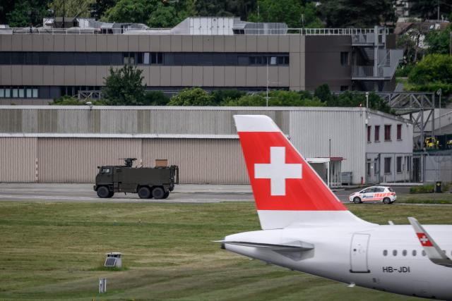 A Swiss Army vehicle and a police car pass behind the tail of a Swiss International Air Lines aircraft during a patrol on the tarmac at Geneva Airport ahead of the upcoming G7 summit in nearby Evian, in Geneva, on June 11, 2026. (Photo by Fabrice COFFRINI / AFP)
