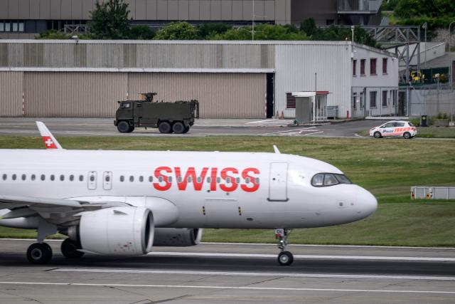 A Swiss Army vehicle and a police car pass behind the tail of a Swiss International Air Lines aircraft during a patrol on the tarmac at Geneva Airport ahead of the upcoming G7 summit in nearby Evian, in Geneva, on June 11, 2026. (Photo by Fabrice COFFRINI / AFP)