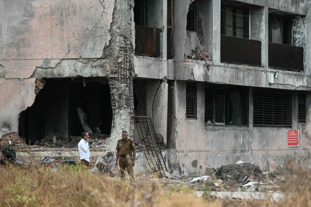 Security personnel stand near a damaged residential building at the site where Air India flight 171 crashed last year, in Ahmedabad on June 11, 2026. India's aviation accident probe agency is facing renewed criticism from pilot groups ahead of the anniversary of the 2025 Air India Boeing-787 crash in Ahmedabad, which killed 260 people. (Photo by Shammi MEHRA / AFP)